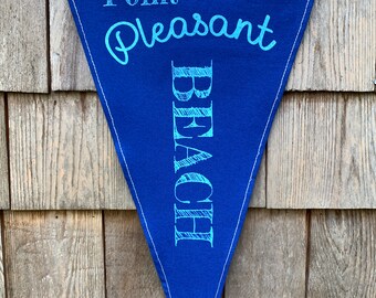 May include: A blue triangular pennant with white trim and the text "Point Pleasant Beach" written in white and light blue lettering.