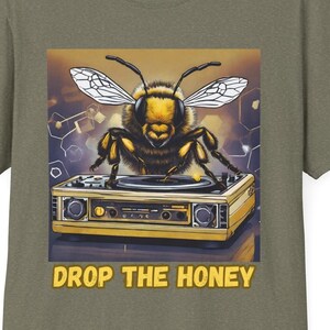 Op de afbeelding: Een gele en zwarte bij met uitgespreide vleugels staat op een vintage draaitafel. De draaitafel is geel en heeft een zwarte plaat erop. De achtergrond is een geel en bruin honingraatpatroon. De tekst "DROP THE HONEY" is in geel onder de draaitafel gedrukt.
