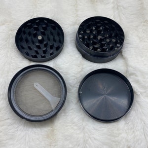 May include: A four-piece black metal grinder with a screen and a small plastic scraper. The grinder has a textured surface and a circular design.