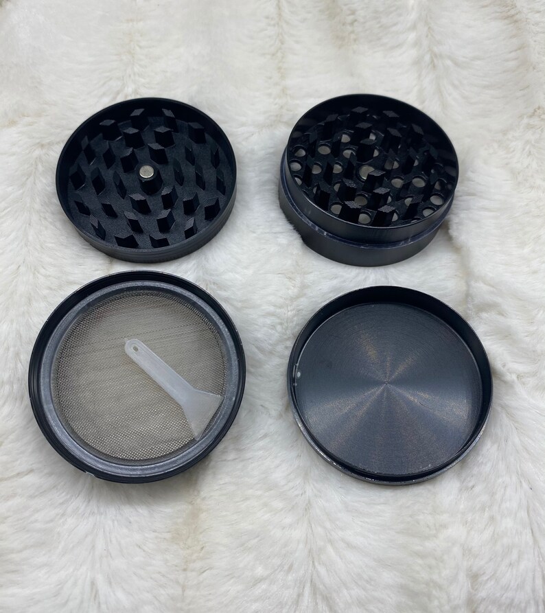 May include: A four-piece black metal grinder with a screen and a small plastic scraper. The grinder has a textured surface and a circular design.