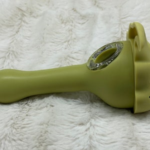 May include: A green silicone smoking pipe shaped like a jack-o'-lantern with a clear glass bowl.