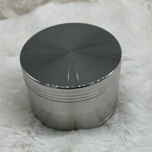 May include: A silver metal grinder with a smooth, shiny finish. The grinder has four sections and a textured top.