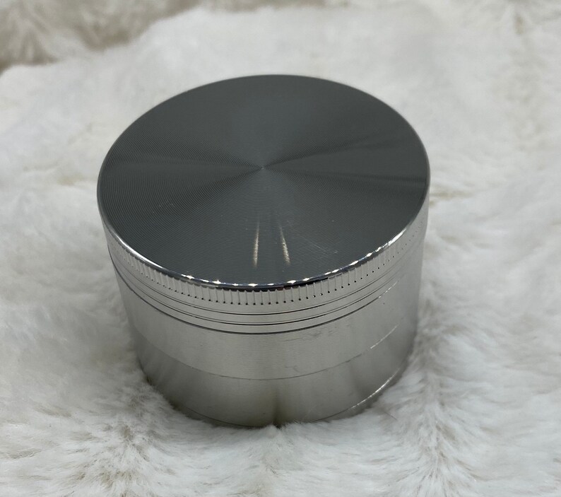 May include: A silver metal grinder with a smooth, shiny finish. The grinder has four sections and a textured top.