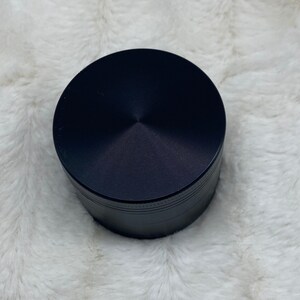 May include: A black metal grinder with a circular top and a textured surface.