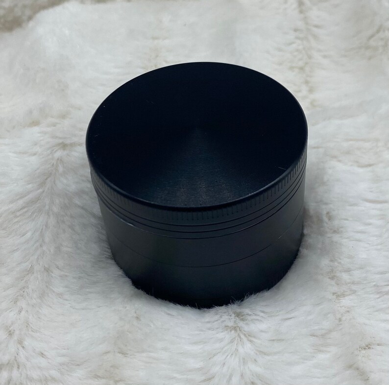 May include: A black metal grinder with a smooth, circular top and a textured, ridged bottom.