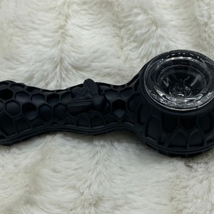 May include: Black silicone pipe with a honeycomb pattern and a clear glass bowl. The pipe features a bee design on the side. The product is designed for smoking herbs.