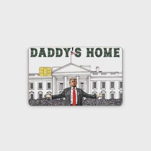 May include: A rectangular credit card skin featuring a line drawing of the White House with a central figure in a suit and red tie standing with arms outstretched. The text DADDY'S HOME is printed in a green camouflage pattern at the top.