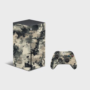 May include: A rectangular gaming console and a wireless controller, both featuring a digital camouflage pattern in shades of black, gray, and beige. The console has a black honeycomb top vent and the Xbox logo, while the controller has buttons.