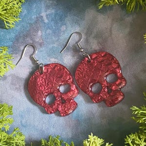 May include: A pair of red skull-shaped earrings with a textured finish. The earrings are made of resin and have silver hooks.