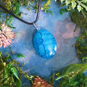 May include: A blue resin pendant necklace with a textured, shell-like design. The pendant is hanging from a black cord.