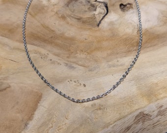 May include: A silver chain necklace with a delicate, cable-link design. The chain is laying flat on a wooden surface.