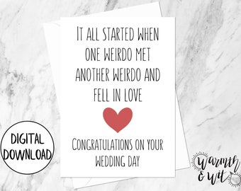 May include: A white card with black text that reads "It all started when one weirdo met another weirdo and fell in love. Congratulations on your wedding day." A red heart is above the text. The card is on a white marble background.