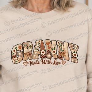 Peut inclure: Un sweat-shirt à col rond beige arborant le mot GRANNY en grandes lettres majuscules à motifs floraux, à carreaux et en forme de cœur. Sous le mot, le texte Made With Love est imprimé en écriture cursive brune avec de petits cœurs.