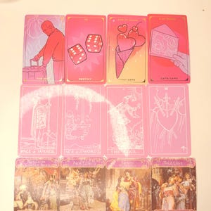 May include: A collection of pink tarot cards with various illustrations and text. The cards feature images of a person with luggage, dice, an ice cream cone with hearts, and an envelope. Other cards show figures and symbols. Text includes "Destiny", "First Date", and "Date Card".
