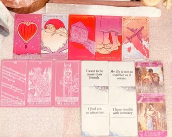 May include: A collection of pink and red tarot cards with various illustrations and text. The cards feature images of a hot air balloon, a woman in clouds, and a box with roses. Some cards have phrases like "I want to be more than friends."