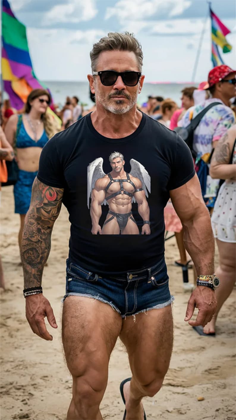 May include: A man wearing a black t-shirt with a graphic of a muscular man with wings and a leather harness. He is also wearing denim shorts and sunglasses.