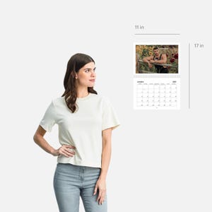May include: A 2023 calendar with a photo of a person in a field of sunflowers. The calendar is 11 inches wide and 17 inches tall.
