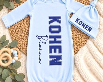 May include: A light blue long-sleeve baby gown with a matching knotted hat. The gown features the name KOHEN in large block letters and Blaine in script. The hat features the name KOHEN in blue block letters on the folded cuff.