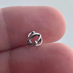 May include: A silver charm with a circular design featuring a knot-like pattern.