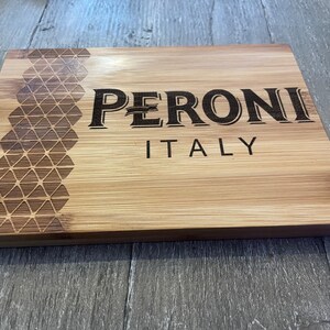May include: A wooden cutting board with a geometric pattern and the text "PERONI ITALY" engraved on the surface.
