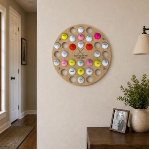 May include: A round wooden golf ball display with 35 holes, each holding a golf ball. The balls are various colors, including white, pink, yellow, and red. The text "BEST DAD BY PAR LOVE EMILY" is engraved on the wood.