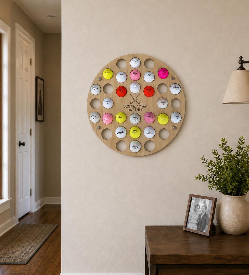 May include: A round wooden golf ball display with 35 holes, each holding a golf ball. The balls are various colors, including white, pink, yellow, and red. The text "BEST DAD BY PAR LOVE EMILY" is engraved on the wood.