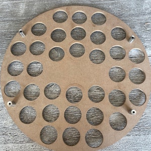 May include: A round, unfinished wooden craft piece with numerous circular cutouts. Four metal posts are evenly spaced around the edge. The wood has a natural, light brown color, and the cutouts are uniform in size and shape.