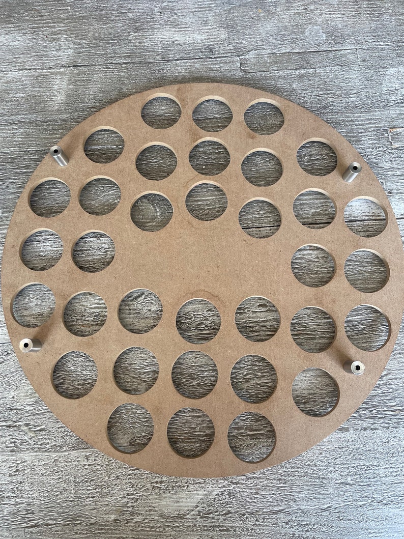 May include: A round, unfinished wooden craft piece with numerous circular cutouts. Four metal posts are evenly spaced around the edge. The wood has a natural, light brown color, and the cutouts are uniform in size and shape.