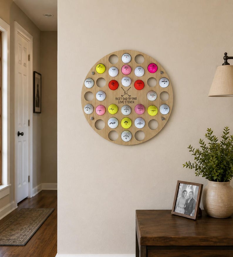 May include: A round, wooden golf ball display with 30 holes, each holding a golf ball. The display has the text "BEST DAD BY PAR LOVE STEVEN" and two crossed golf clubs. The golf balls are various colors.