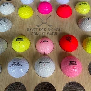 May include: A wooden golf ball display stand with multiple golf balls in various colors. The stand has the text "BEST DAD BY PAR LOVE STEVEN" engraved on it. Golf balls include brands like Slazenger, TaylorMade, and Volvik.