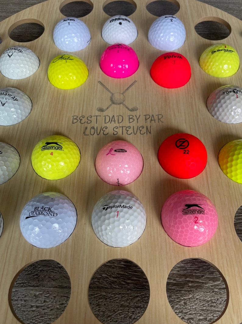 May include: A wooden golf ball display stand with multiple golf balls in various colors. The stand has the text "BEST DAD BY PAR LOVE STEVEN" engraved on it. Golf balls include brands like Slazenger, TaylorMade, and Volvik.