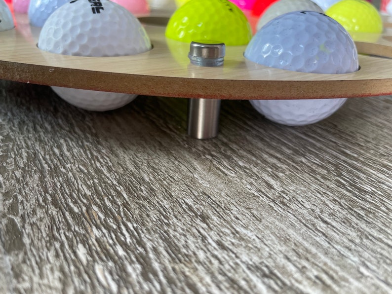 May include: A wooden golf ball display stand with multiple golf balls in various colors. The stand has a light wood finish and a metal support. The golf balls are white, yellow, pink, and blue.