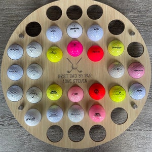 May include: A round wooden golf ball display with 28 golf balls in various colors and brands. The display has the text "BEST DAD BY PAR LOVE STEVEN" and a golf club graphic.