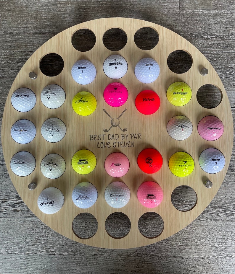 May include: A round wooden golf ball display with 28 golf balls in various colors and brands. The display has the text "BEST DAD BY PAR LOVE STEVEN" and a golf club graphic.