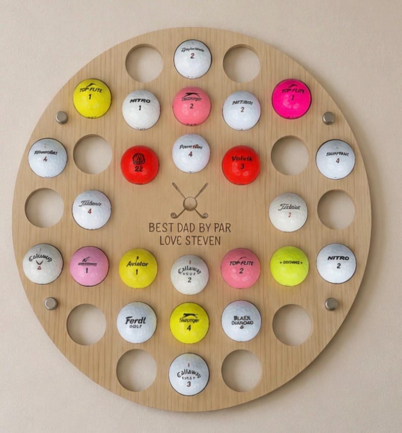 May include: A round wooden golf ball display with 28 golf balls of various colors and brands. The display has a circular design with holes to hold the balls. Text on the display reads "BEST DAD BY PAR LOVE STEVEN."