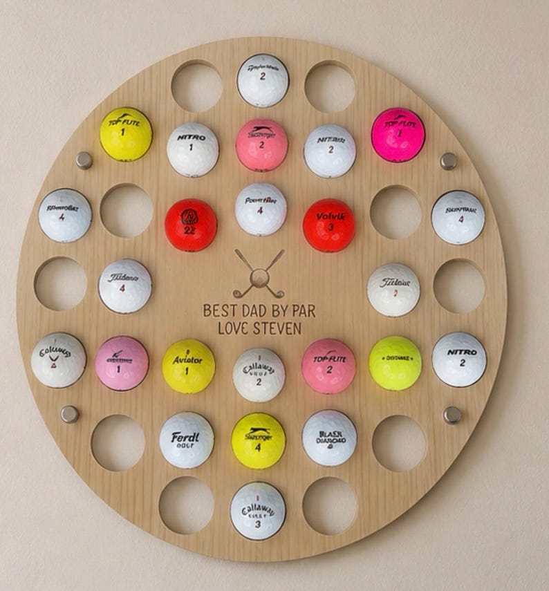 May include: A wooden golf ball display with a circular design. It features numerous holes holding golf balls of various colors, including yellow, pink, and white. The text "BEST DAD BY PAR LOVE STEVEN" is engraved on the wood.