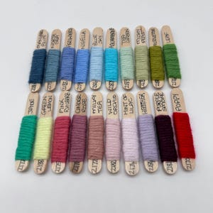 May include: A collection of yarn samples on wooden sticks, each labelled with a colour name and number. The colours include blue, green, pink, red, brown, beige, purple, and more.