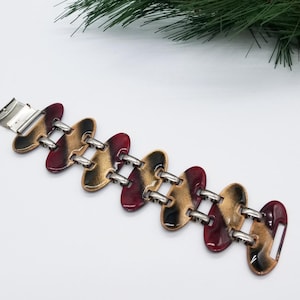 May include: A silver and gold tone bracelet with red and black enamel accents. The bracelet is made of linked oval-shaped pieces.