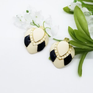 May include: A pair of vintage clip-on earrings. Each earring has a cream-coloured teardrop shape at the top, framed in gold-tone with small clear rhinestones. The lower section features a black and cream checkerboard pattern.