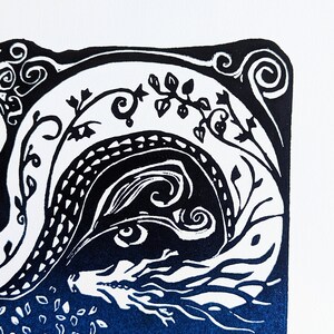 May include: Black and white linocut print of a dragon with blue ink. The dragon is curled up with its head and eyes visible. The background is a dark blue colour with white details.