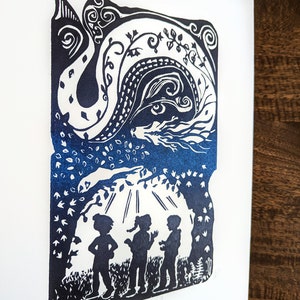 May include: A blue and white linocut print of three children standing in a forest with a dragon in the sky above them. The print is titled "Imagine Beyond".