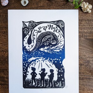 May include: A blue and white linocut print of a dragon with three children standing beneath a tree. The print is titled "Imagine Dragons II" and is signed and numbered.
