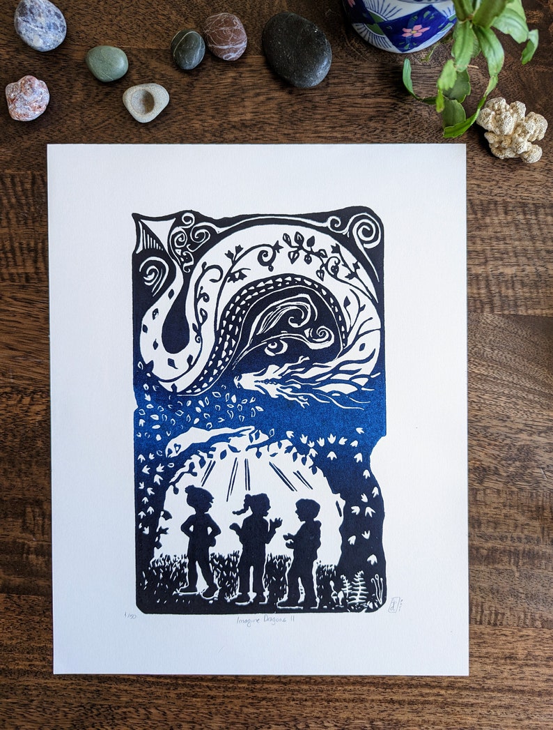 May include: A blue and white linocut print of a dragon with three children standing beneath a tree. The print is titled "Imagine Dragons II" and is signed and numbered.