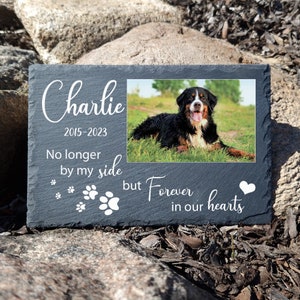 May include: Black and white photo of a dog in a photo frame on a black slate plaque. The plaque reads "Charlie 2015-2023 No longer by my side but Forever in our hearts".