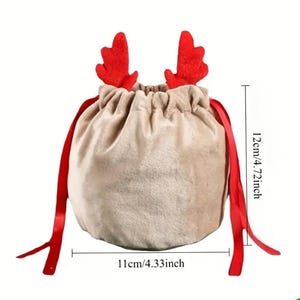May include: A beige velvet drawstring gift bag with red reindeer antlers and red ribbon ties. The bag is 11cm wide and 12cm tall, ideal for festive presents.