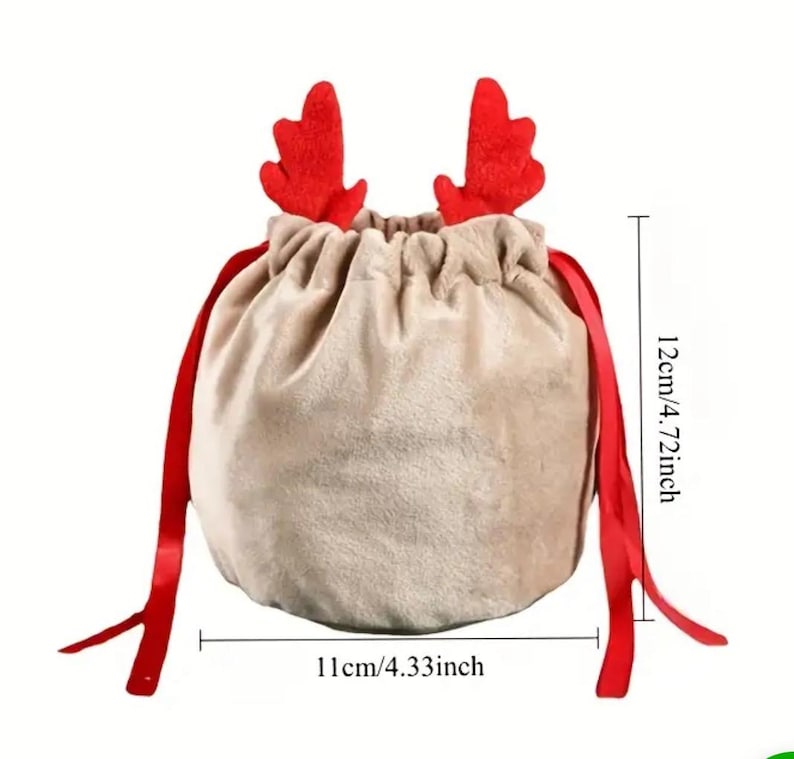 May include: A beige velvet drawstring gift bag with red reindeer antlers and red ribbon ties. The bag is 11cm wide and 12cm tall, ideal for festive presents.