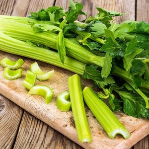 Puede incluir: Un manojo de tallos de apio verde fresco con hojas en una tabla de cortar de madera. El apio se ha cortado en trozos y está listo para usarse en una receta.
