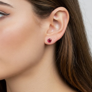 May include: A pair of ruby red stud earrings. The earrings are small and round, and they are set in a silver setting.