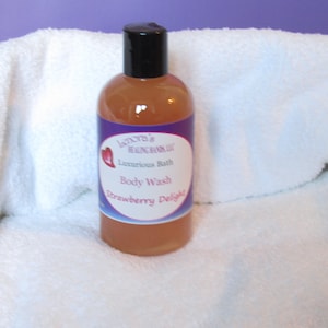 May include: A clear bottle of body wash with a black cap, labeled "Lenore's Healing Hands LLC." The label reads "Luxurious Bath Body Wash Strawberry Delight." The bottle is on a white towel, with a purple background.