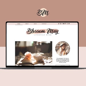 May include: A laptop computer displaying a website with the title "Blossom May Lifestyle Blog". The website features a photo of a cup of tea and a pink flower on a bed, and a photo of a woman wearing a hat and smiling. The text "I'm a paragraph. Click here to add your own text and edit me. It's easy. I'm a paragraph. Click here to add your own text and edit me. It's easy." is displayed on the website.